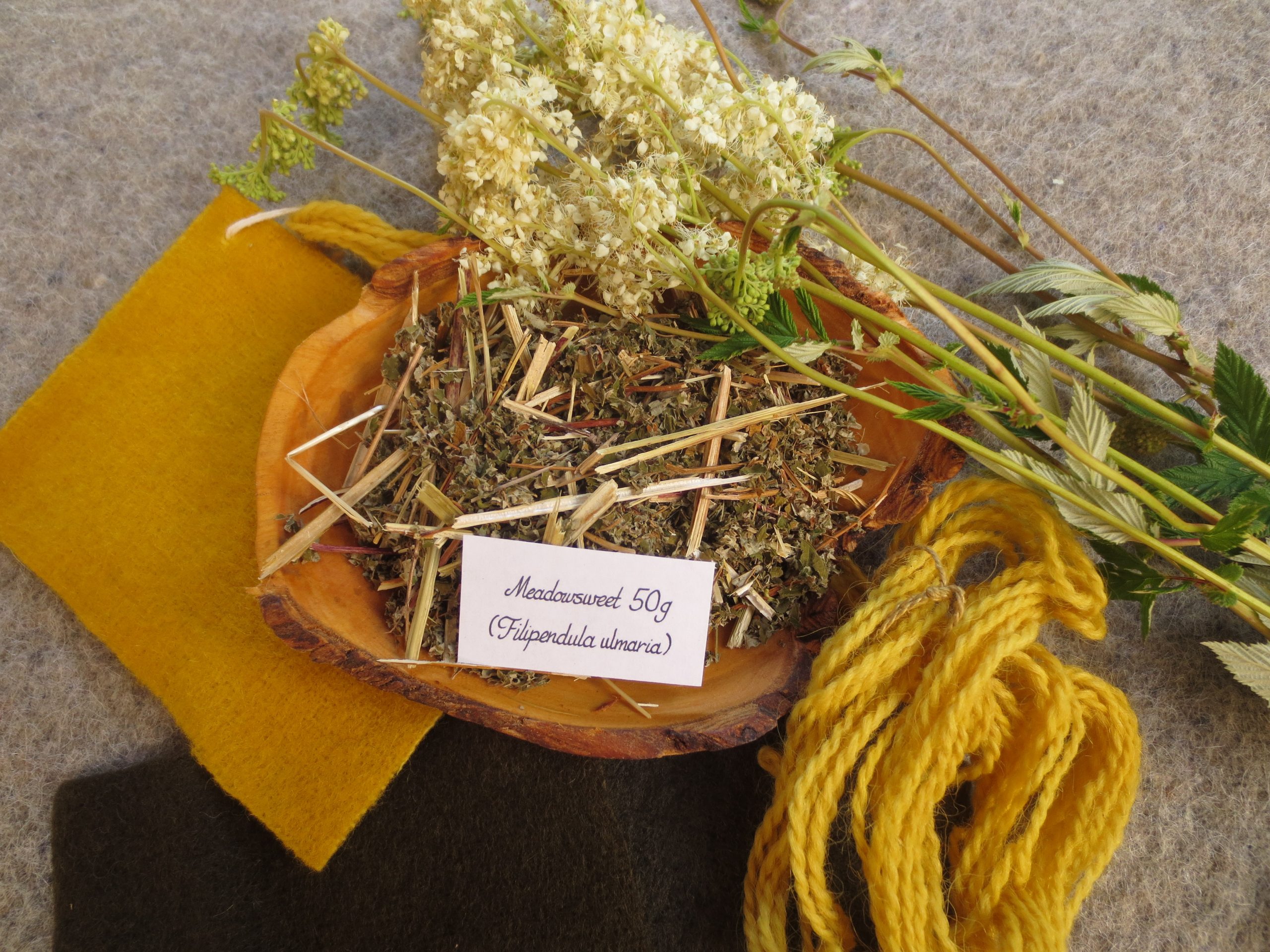 Bowl of dried meadowsweet and swatches of yellow and dark grey brown wool fabric