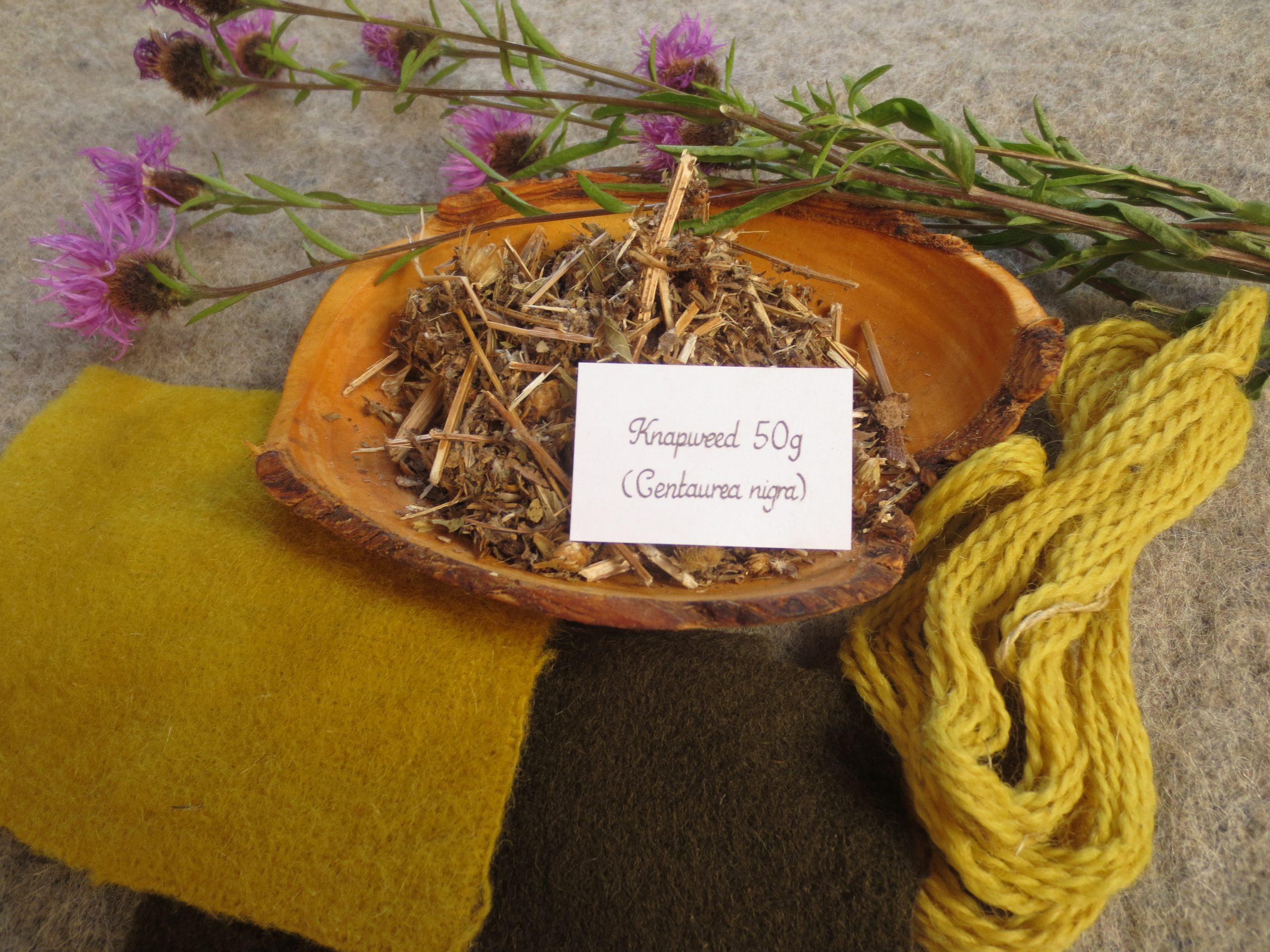 Bowl of dried knapweed and wool swatch samples in yellow and greyish green