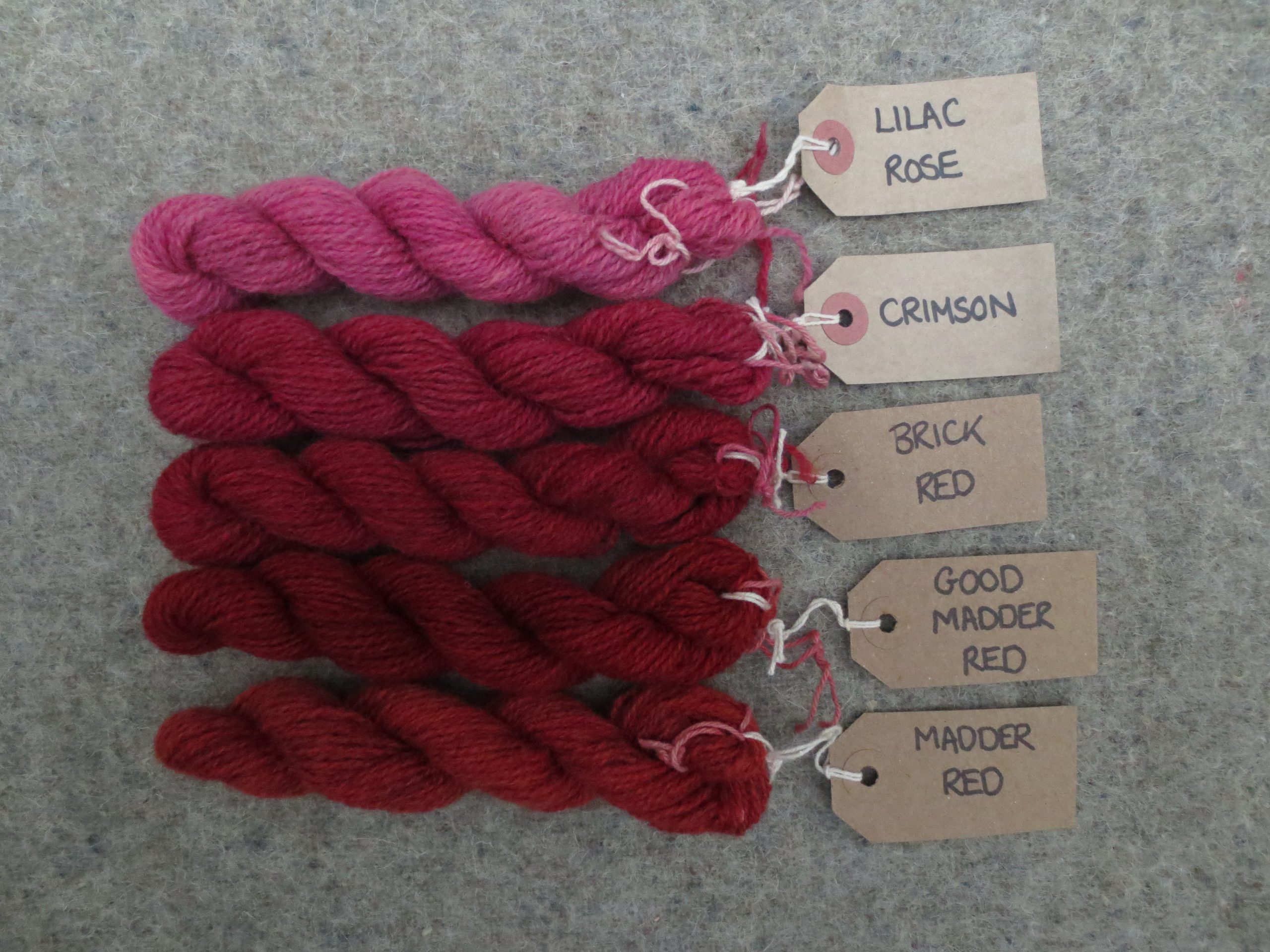 5 wool skeins labelled lilac rose, crimson, brick red, good madder red and madder red