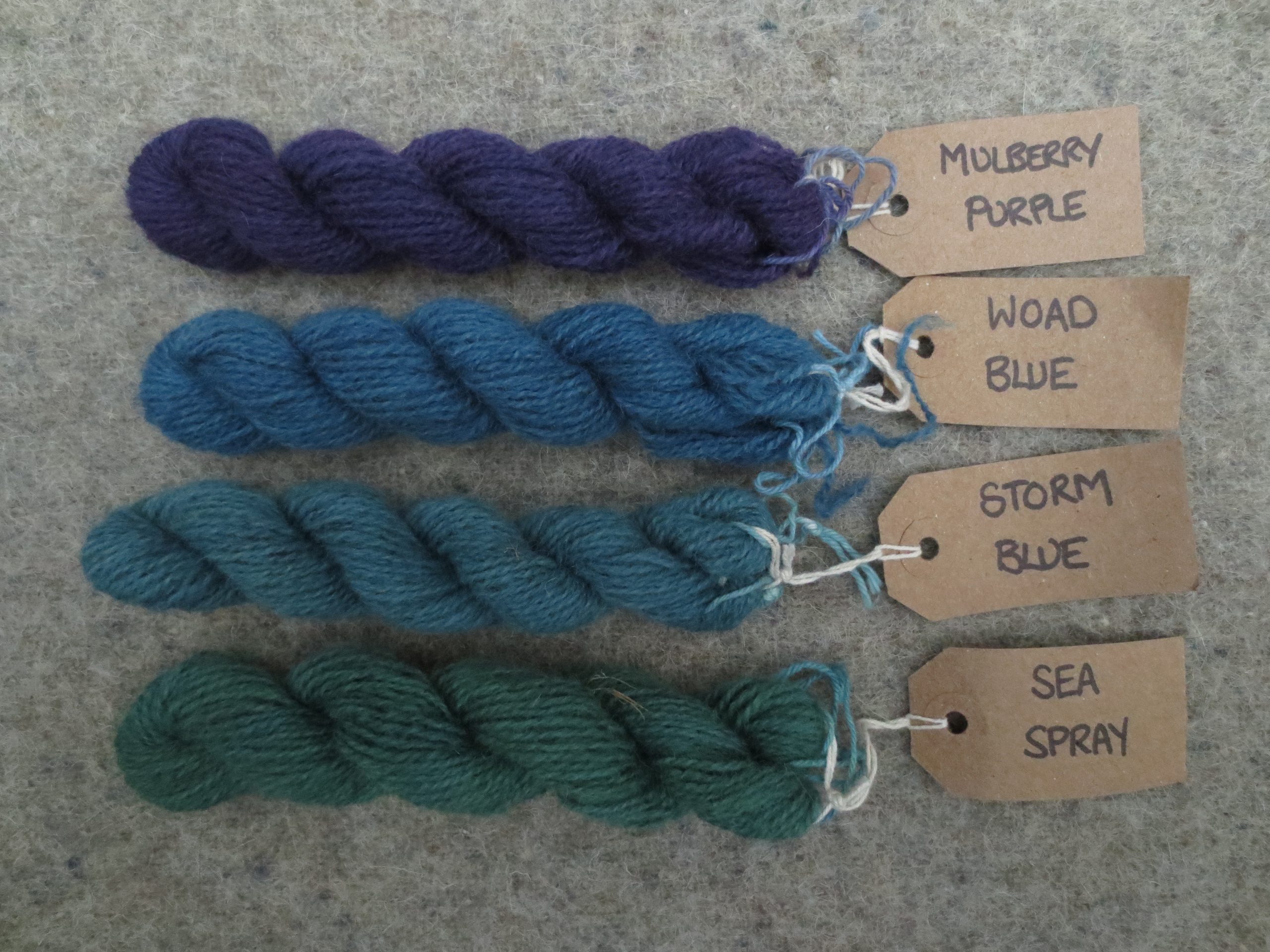 4 wool skeins labelled mulberry purple, woad blue, storm blue and sea spray