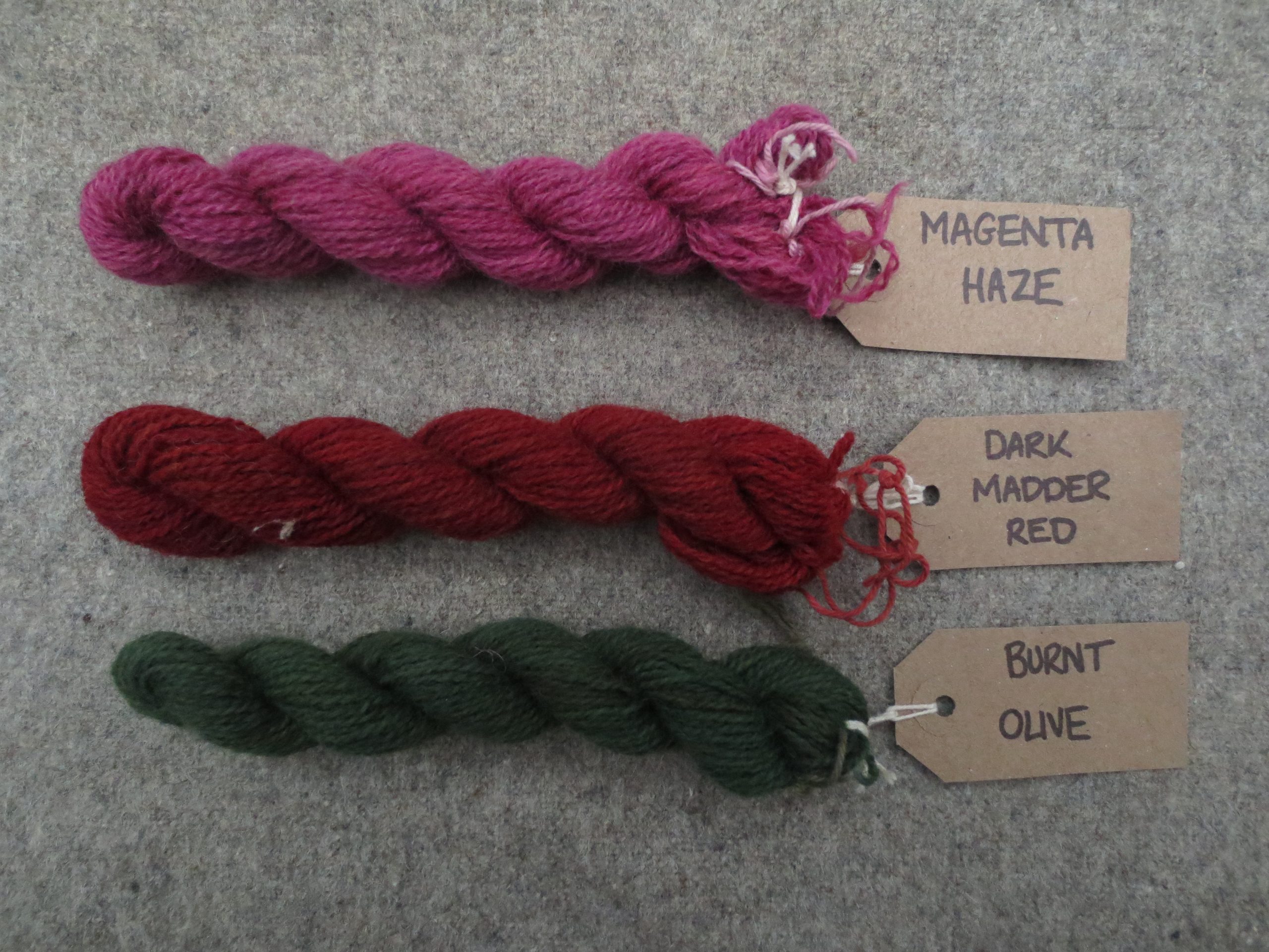3 skeins of wool labelled magenta haze, dark madder red and burnt olive
