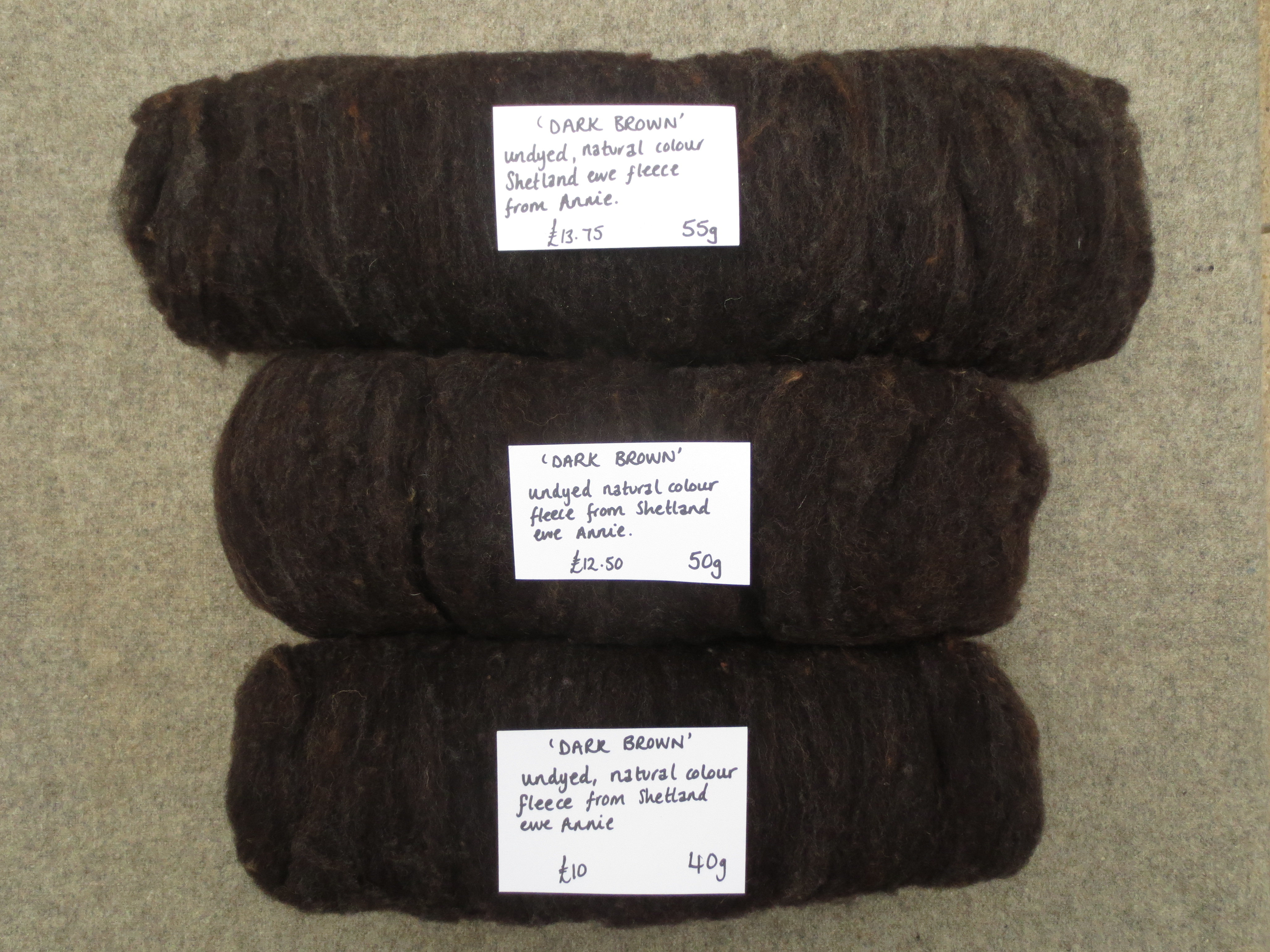 3 carded batts of wool rolled up and labelled Dark Brown 55g, 45g and 40g